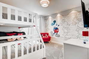 Habitación infantil con literas, una silla roja y un mural de Mickey Mouse.