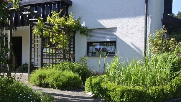 Een wit gebouw met een tuininloop, een houten pergola en een raam met uitzicht op de tuin.