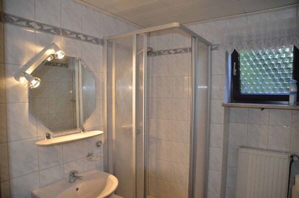 Un baño con ducha de vidrio, lavamanos con espejo y ventana con persiana decorada.