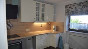 Een compacte keuken met witte kastjes, een houten aanrecht, een koffiezetapparaat en een raam met uitzicht op groen.