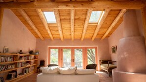 A cozy room with a wooden ceiling, a white sofa, a bookshelf, and a large window. - Peaceful family/group home with private attached treehouse (Canones)