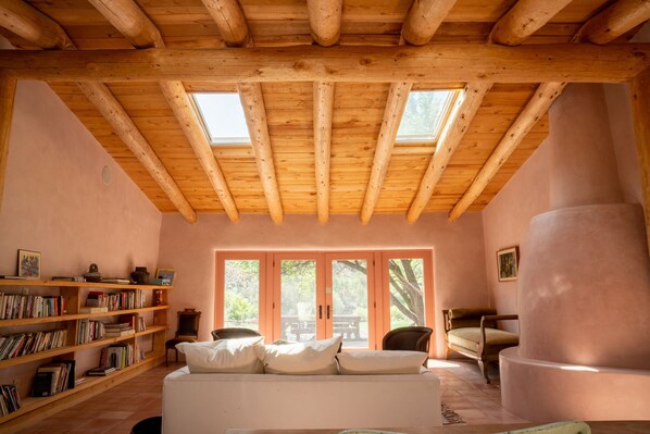 A cozy room with a wooden ceiling, a white sofa, a bookshelf, and a large window.