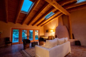 A cozy room with a wooden ceiling, a white sofa, and a large window overlooking a garden.