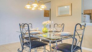 Un coin repas avec une table en verre et des chaises en métal, un vase rempli de fleurs et un lustre.