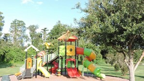 Un terrain de jeux avec des toboggans et des structures d’escalade, entouré d’arbres et d’herbe.