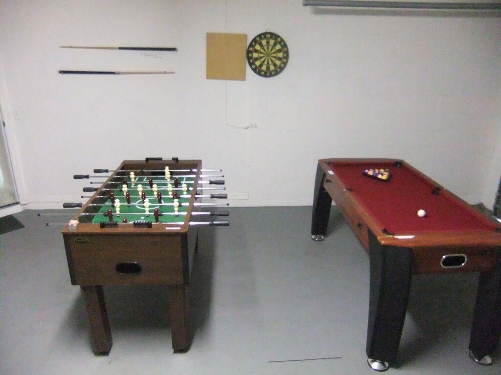 A room with a foosball table, a pool table, and two dartboards on the wall.