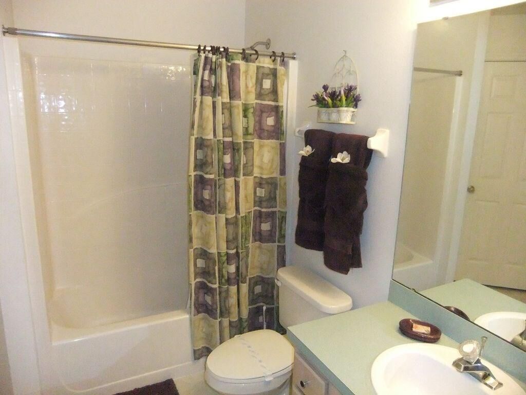 A bathroom with a shower curtain, toilet, sink, and a mirror.