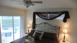 A bedroom with a bed, two bedside lamps, a ceiling fan, a window with blinds, and a view of the outdoors. - Ref 03 Luxury 4 Bed Villa With Lake View own Pool (Kissimmee)