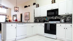 A modern kitchen with white cabinetry, a black microwave, and a tiled backsplash. - Ref 07 Modern 5 Bed Villa With own Pool Near Disney (Kissimmee)
