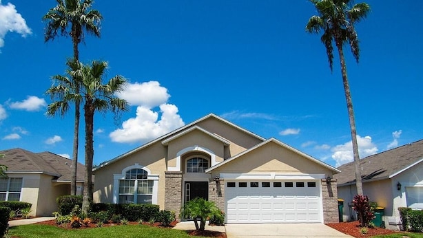 A single-story house with a front garage, a small front porch, and a well-maintained lawn with palm trees. - Ref 07 Modern 5 Bed Villa With own Pool Near Disney (Kissimmee)