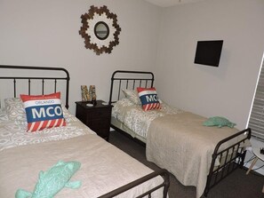 A room with two beds, each with a pillow and a blanket. There is a small table with a lamp and a decorative item on it. - Ref 09 Luxury 4 Bed Villa With Private Pool and Lake View (Kissimmee)