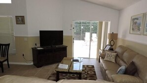 Ein Wohnzimmer mit einer Couch, einem Couchtisch, einem Fernseher auf einem Schrank und einer Tür, die nach draußen führt.