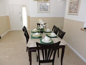 A dining area with a rectangular table set for six, surrounded by six chairs. The table is covered with a green placemat and white tablecloth. There are two framed pictures on the wall above the table. - Ref C Luxury 4 Bed Villa on Gated Resort Near Disney (Kissimmee)