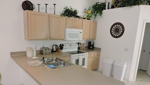 A kitchen with light wooden cabinets, a white microwave, a stove, and a sink. There are plants on the cabinets and a decorative wall piece. - Ref D Stunning 4 Bed Villa With own Pool spa Near Disney (Kissimmee)