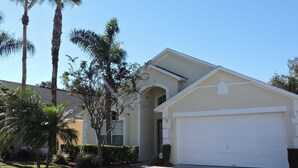 A single-story house with a white garage door, surrounded by palm trees and a well-maintained lawn. - Ref D Stunning 4 Bed Villa With own Pool spa Near Disney (Kissimmee)