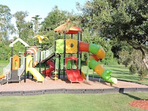 Explore a playground with slides and climbing elements set amidst a lush green area and trees.