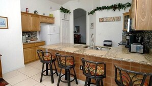 A kitchen with a central island, wooden cabinets, a refrigerator, and a sink. There are three bar stools with floral cushions. - Ref E Luxury 4 Bed Villa With Private Pool Near Disney (Kissimmee)