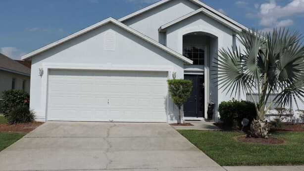 A two-story house with a white garage door, a front entrance with a small porch, and a palm tree in the front yard. - Ref E Luxury 4 Bed Villa With Private Pool Near Disney (Kissimmee)