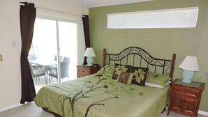 A bedroom with a bed, two nightstands, a window with blinds, and a view of an outdoor area.