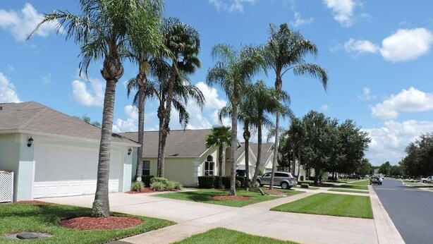 A residential street with houses, palm trees, and a clear sky.