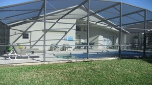 A covered outdoor area with a pool, lounge chairs, and a grill.
