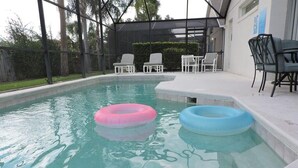 A swimming pool with two inflatable rings, surrounded by a covered patio with chairs and tables.