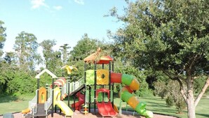 Un parque infantil con toboganes y estructuras para escalar, rodeado de árboles y césped.