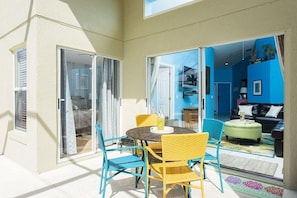 A sunlit patio with a round table and chairs, a sliding glass door leading to a living area with a sofa and a coffee table. - Ref 18 Stunning 4 Bed Villa With own South Facing Pool (Kissimmee)