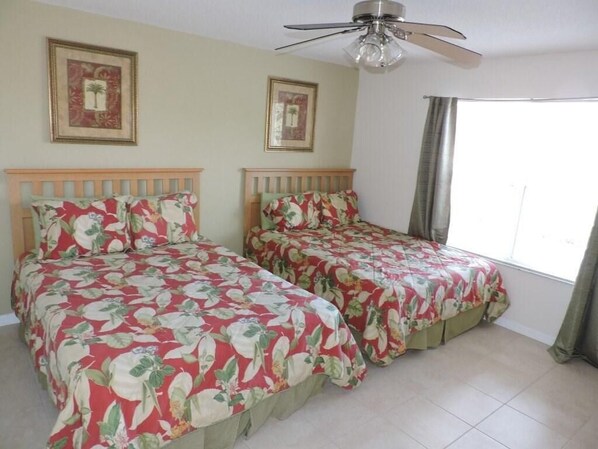 A room with two beds, a ceiling fan, and framed pictures on the wall.