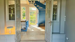 Un couloir doté d’un plancher en bois, d’un escalier bleu et d’une porte donnant sur une pièce avec une fenêtre.