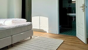 Une chambre à coucher avec un lit, une porte blanche et une salle de bain visible à travers une porte ouverte.