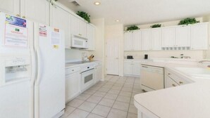 A kitchen with white cabinets, a microwave, and a refrigerator. There are signs on the refrigerator and cabinets.