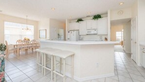 A spacious kitchen with a central island, white cabinetry, and a dining area with chairs and a table.