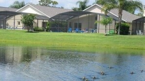 A building with a covered outdoor area, a pond with ducks, and a grassy lawn. - Ref 01 Stunning 4 Bed Villa With own Pool Spa Lake View (Kissimmee)