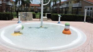 A water fountain with multiple jets and decorative elements, surrounded by a paved area with a fence and residential buildings in the background. - Ref 01 Stunning 4 Bed Villa With own Pool Spa Lake View (Kissimmee)