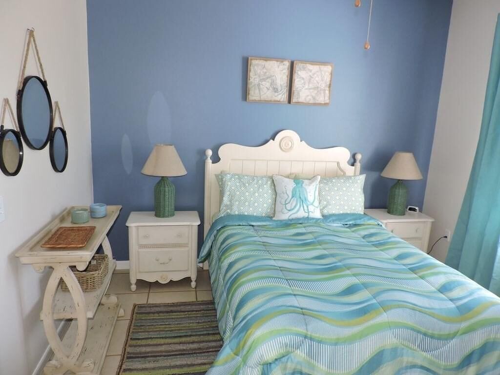 A bedroom with a bed, two nightstands, a lamp, a wall-mounted mirror, and a blue wall.