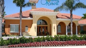 A two-story building with a red-tiled roof, a central entrance with an archway, and palm trees in the foreground. - Ref 37 Beautiful 6 Bed Villa With Pool Gated Resort (Davenport)
