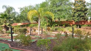 A miniature golf course with a green putting surface, red borders, and various plants and trees in the background. - Ref 37 Beautiful 6 Bed Villa With Pool Gated Resort (Davenport)