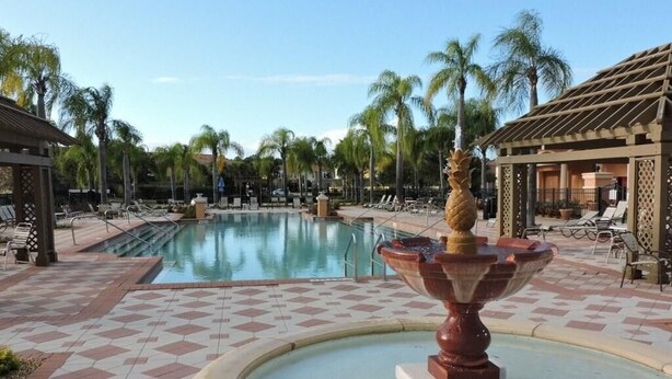 A pool area with a central fountain, lounge chairs, palm trees, and a tiled walkway. - Ref 01bv Stunning 5 Bed 4 Bath Villa With own Pool (Kissimmee)