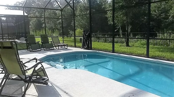 A swimming pool with a covered area, surrounded by chairs and a fence.