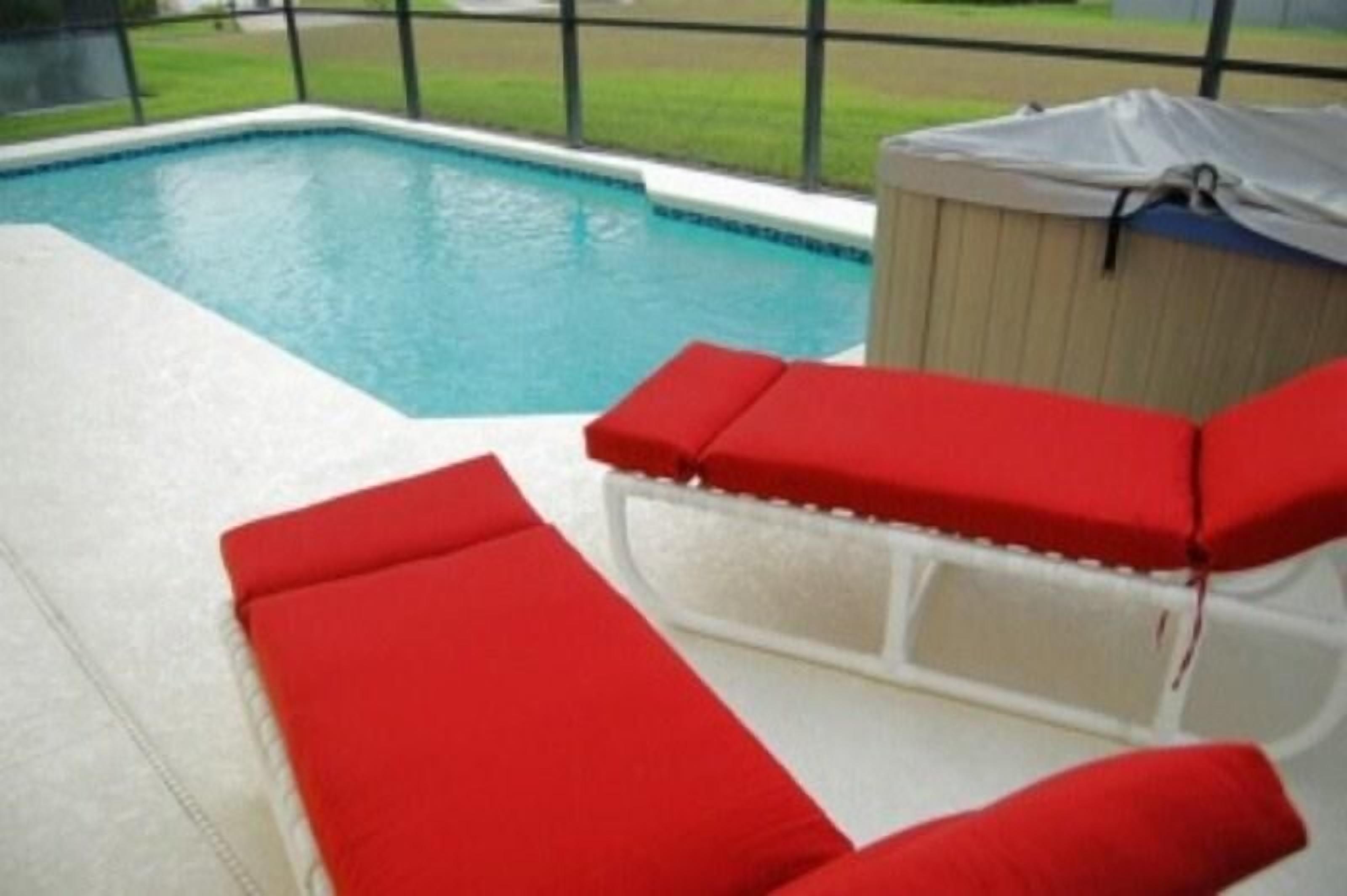 A pool area with a hot tub and red lounge chairs.