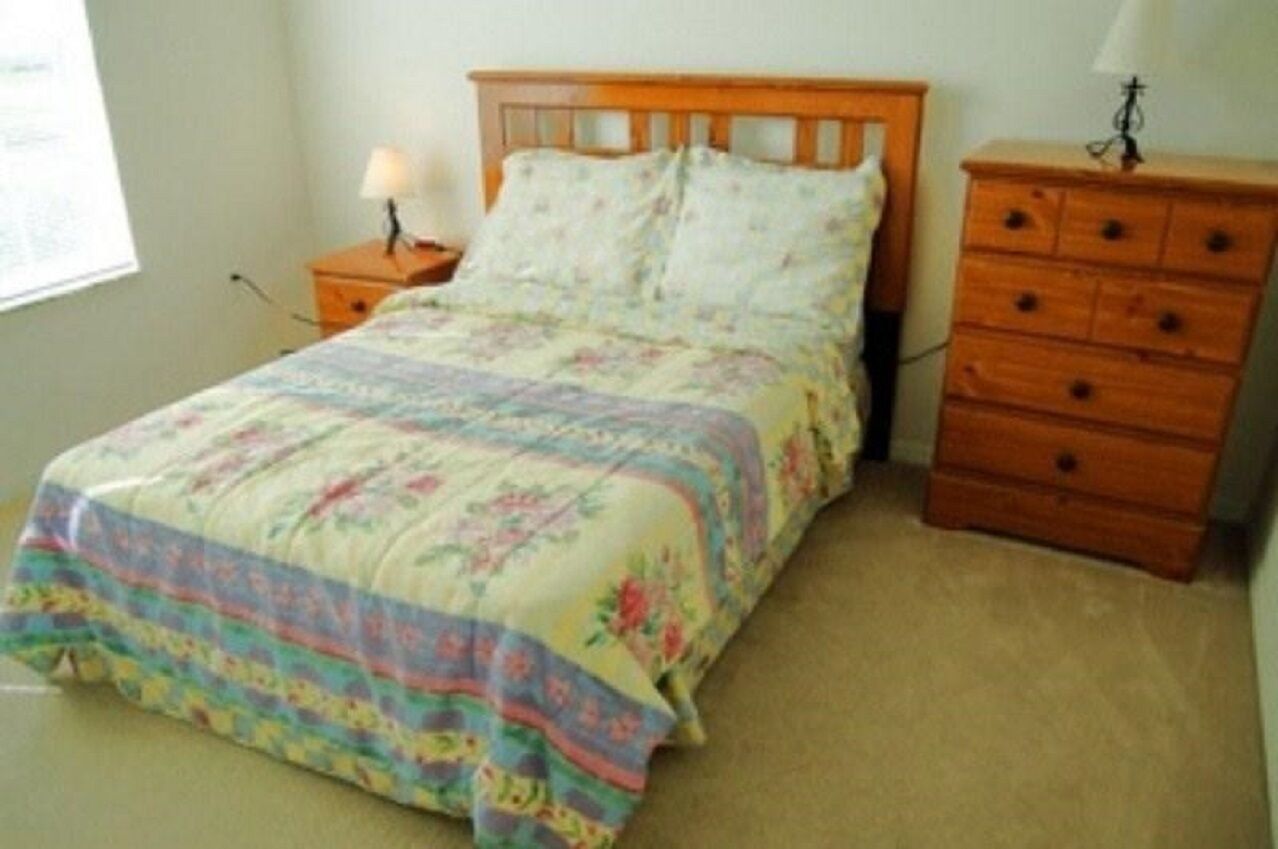 A bedroom with a bed, a nightstand, a dresser, and a lamp.