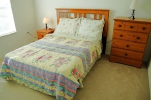 A bedroom with a bed, a nightstand, a dresser, and a lamp.