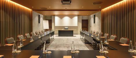 Un salón de conferencias con largas mesas, sillas y botellas de agua.