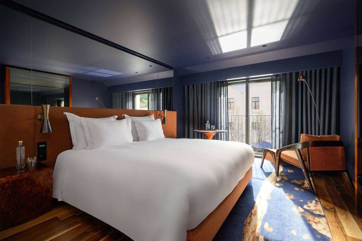 Une chambre d’hôtel moderne avec un grand lit, une petite table avec une chaise, un balcon avec des rideaux et une grande fenêtre.