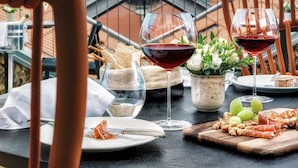 Una mesa con una copa de vino, tabla de quesos y pan, con vistas a un paisaje urbano.