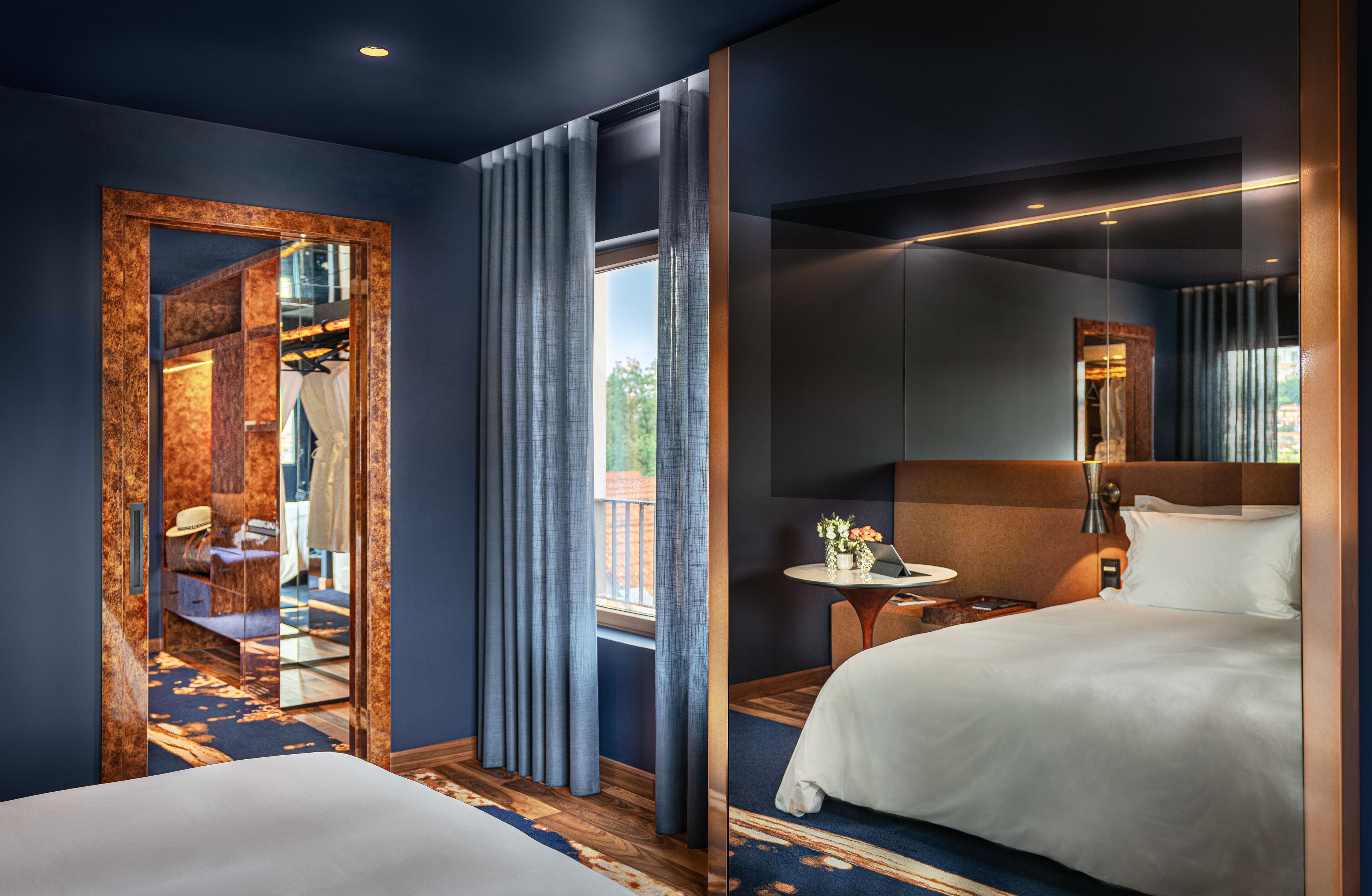 Habitación de hotel con un espejo grande, una cama, una mesita de noche con lámpara y vistas al exterior.