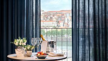 Ein Tisch mit Champagnerflasche, Gläsern, einer Obstschale und Topfpflanzen an einem Fenster mit Blick auf die Stadt.