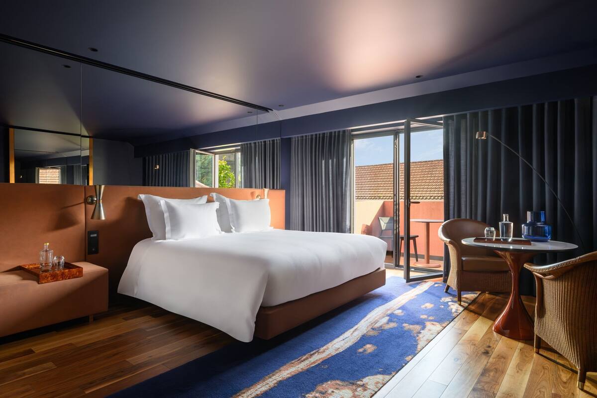 Une chambre d’hôtel moderne dotée d’un grand lit, d’un coin salon avec une table et d’un balcon avec des rideaux.