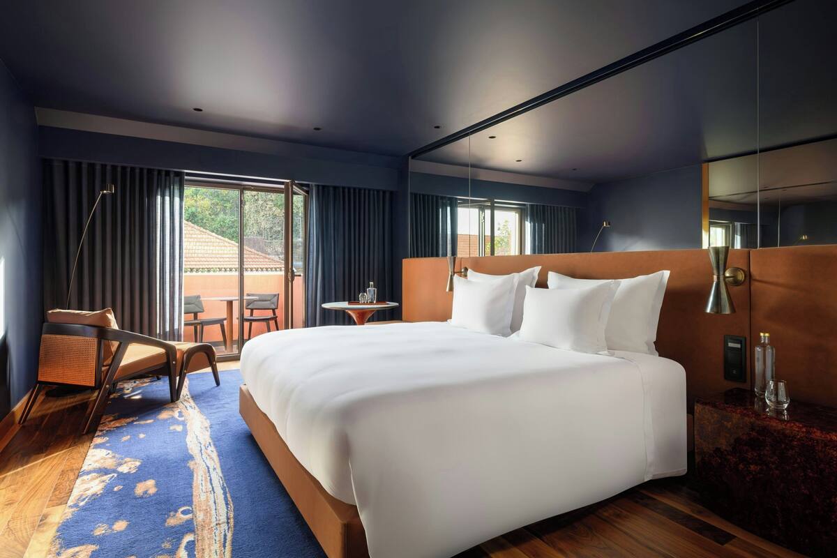 Une chambre d’hôtel moderne dotée d’un grand lit, d’un coin salon avec une chaise et une table, et offrant une vue sur l’extérieur.
